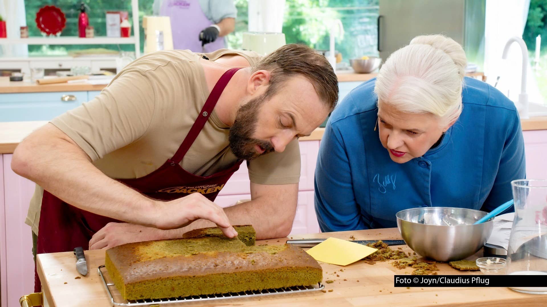 Gleich zwei „Bäcker der Woche“ gehen am 2. September mit roten Schürzen in die neue Folge von „Das große Backen“. Einer von ihnen ist der frühere Handballprofi Andre, der auch diesmal wieder Jurorin Bettina Schliephake-Burchardt und deren Kollegen Christian Hümbs überzeugen will. (Foto © Joyn/Claudius Pflug)